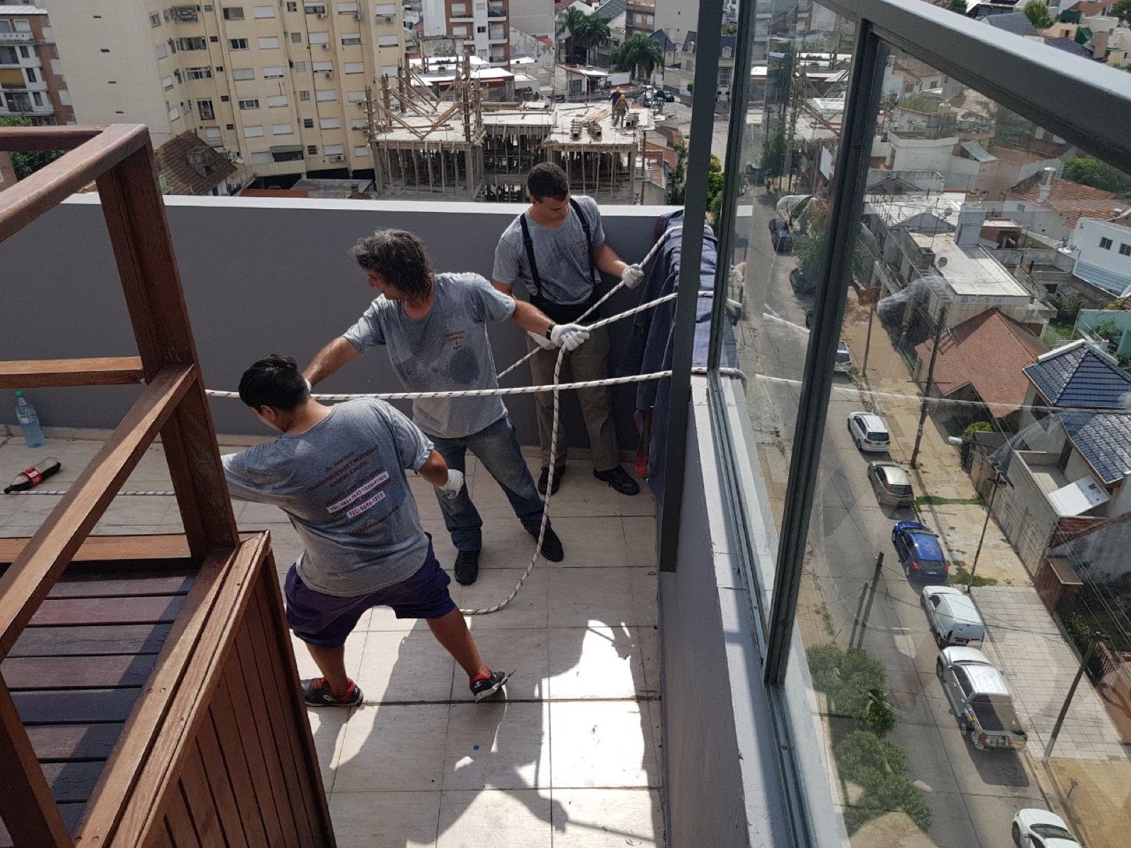 Tres operarios maniobrando las sogas desde el balcón de un piso alto